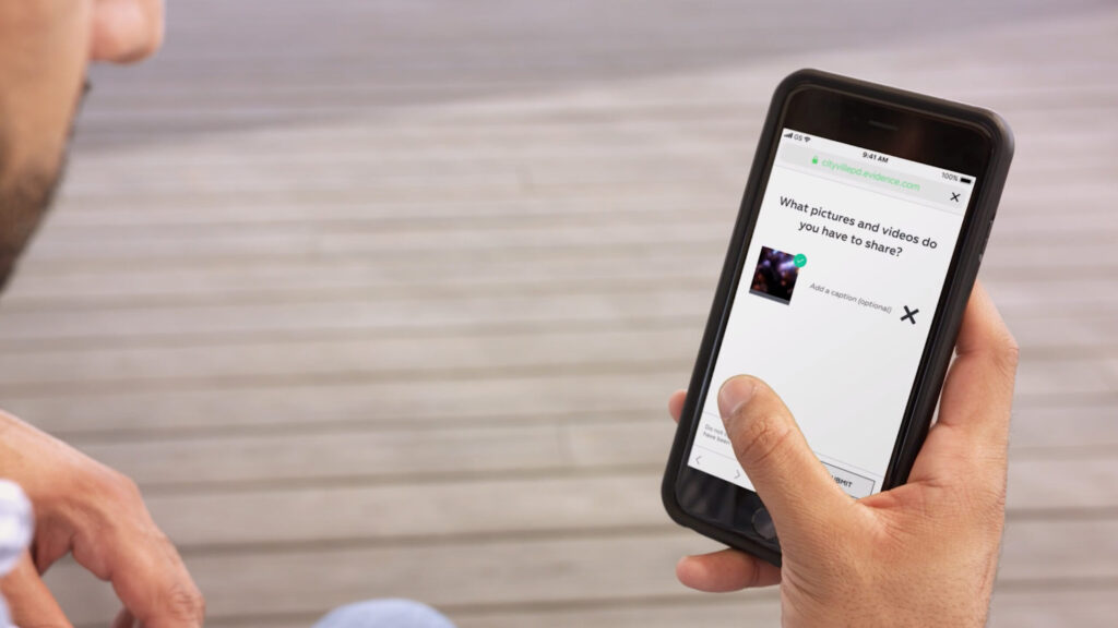 A man holding a cell phone, using the AXON Community App to upload content to DEMS.